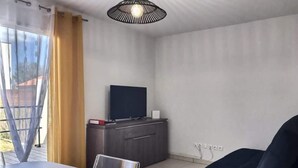 Un salon moderne avec une table blanche, un fauteuil sombre et un téléviseur posé sur un meuble en bois.