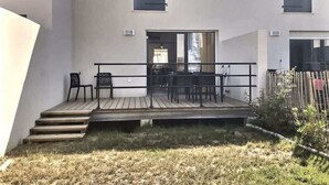 Un bâtiment moderne doté d’un toit plat, d’une terrasse en bois avec des sièges extérieurs et d’un petit jardin.