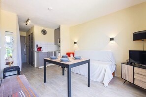 Una habitación moderna con una mesa de comedor para cuatro personas, un sofá, un televisor y una cocina al fondo.