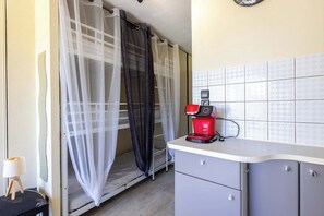 Una kitchenette pequeña con cafetera, una cama con mosquitero y una mesita con lámpara.