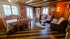 Een gezellige kamer met een houten vloer, een eettafel met stoelen, een bank, een klein bijzettafeltje en een lamp.