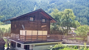 Een houten chalet met balkon, met een bebost berglandschap op de achtergrond.