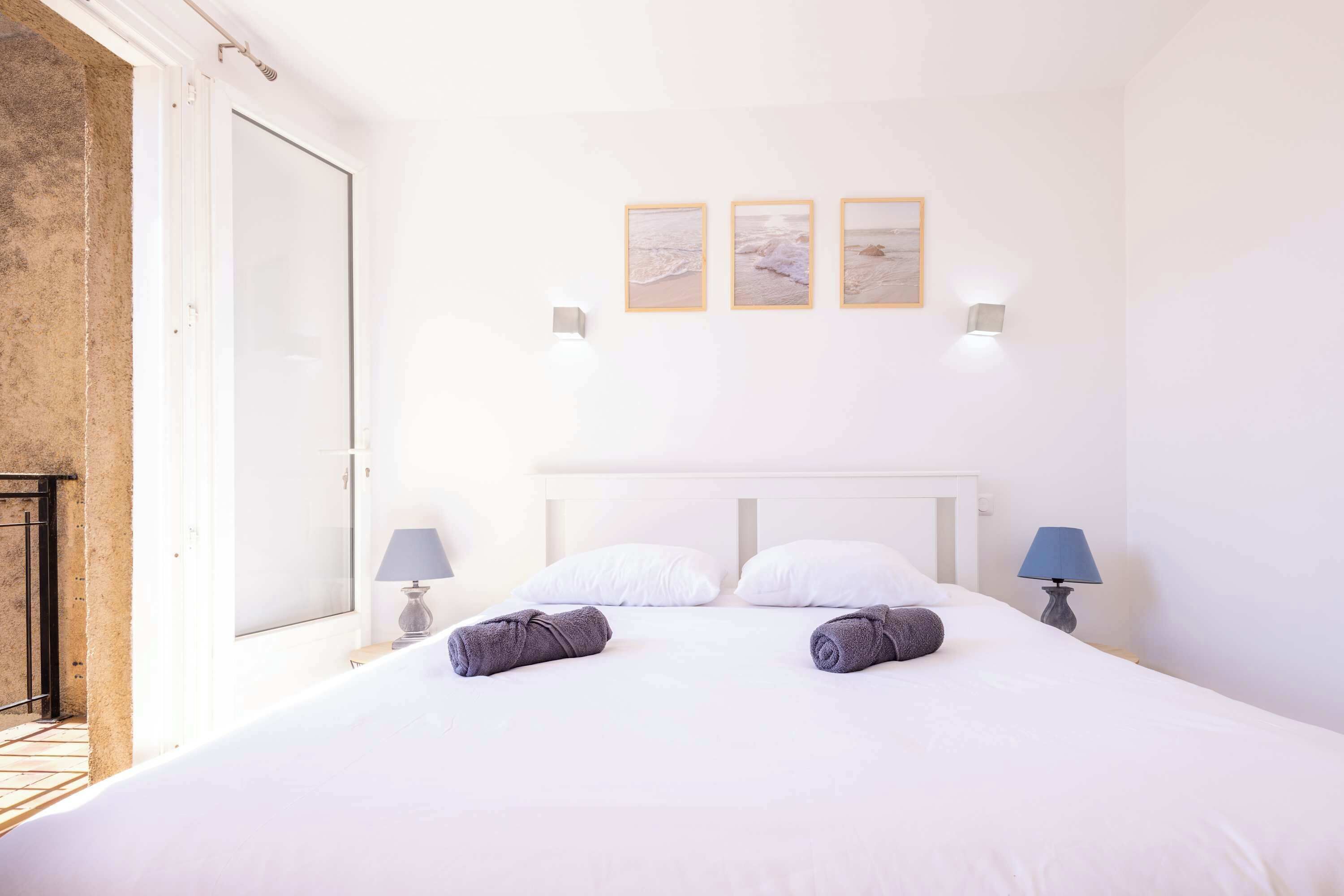A hotel room with a bed, two wall-mounted lamps, and three framed pictures on the wall.