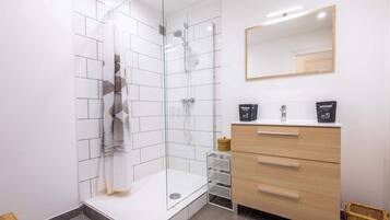 Een moderne badkamer met een douchecabine van glas, een houten wastafelmeubel met een spiegel en een vloer van witte tegels.