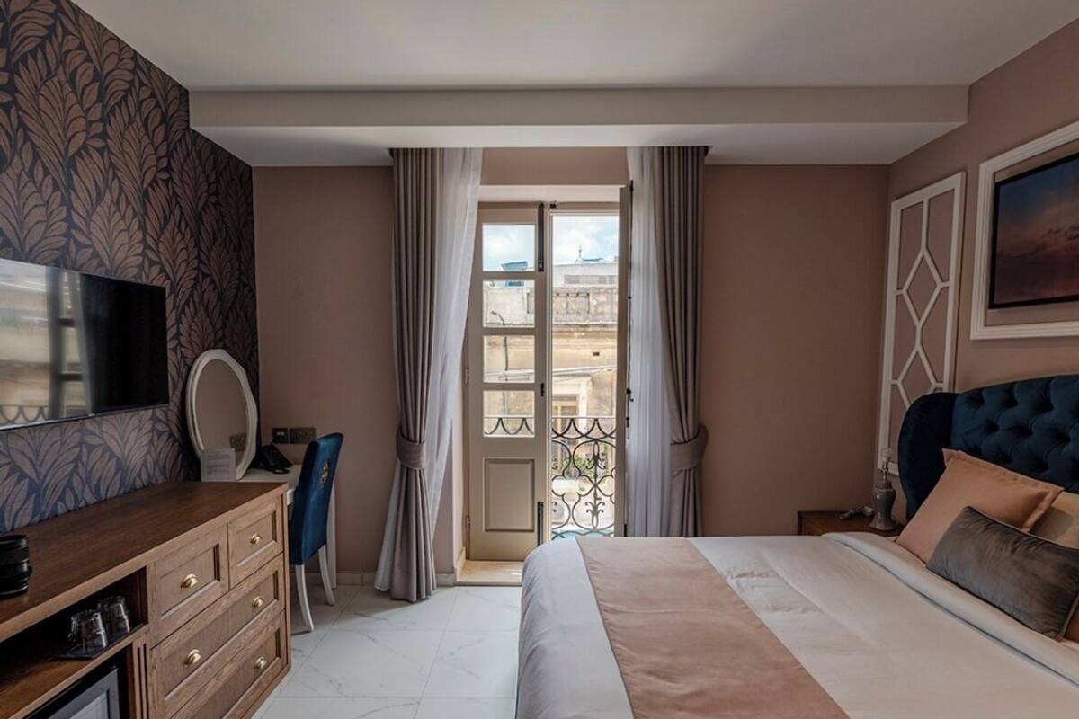 A bedroom with a large bed, a TV, a desk, and a balcony view.