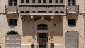 A historic building with a symmetrical facade, featuring a central entrance with an ornate archway, a balcony with wrought iron railings, and a sign indicating a garage. - Palazzo De La Sengle Boutique Hotel (Senglea)