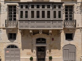 Um edifício histórico com fachada simétrica, apresentando uma entrada central com arco ornamentado, varanda com grades de ferro forjado e uma placa indicando uma garagem.