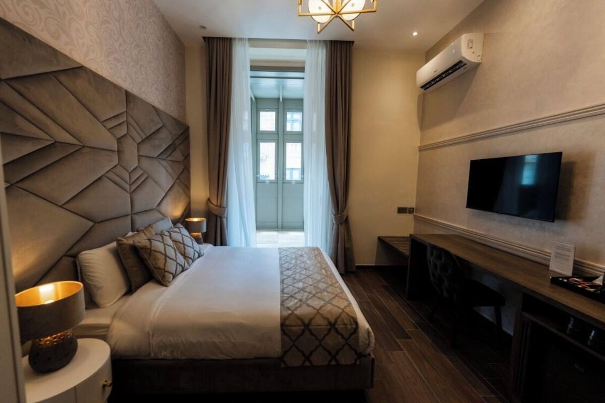 A hotel room with a large bed, a flat-screen TV, an air conditioning unit, and a view of the outdoors.