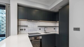 Une cuisine moderne avec des meubles de couleur sombre, un plan de travail blanc et un four en acier inoxydable.