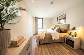 A modern bedroom with a bed, bedside table, lamp, and a large potted plant. - Alameda - Campus Accommodation (Wembley)