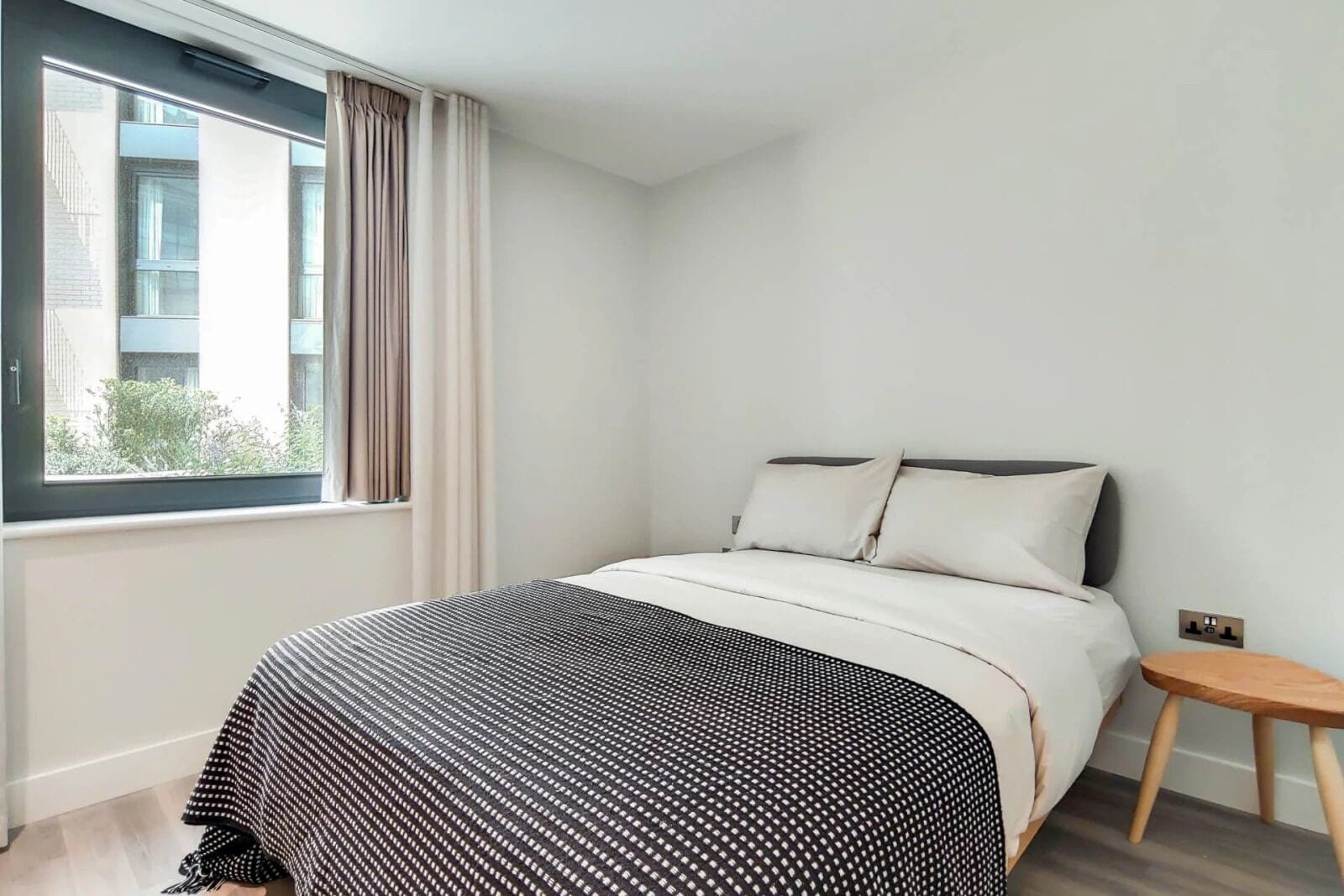 A modern bedroom with a large bed, a small wooden side table, and a window with curtains.