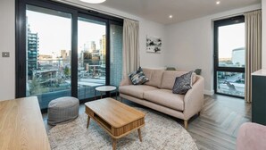 Un salon moderne avec un canapé, une table basse et une vue sur la ville grâce à de grandes fenêtres.