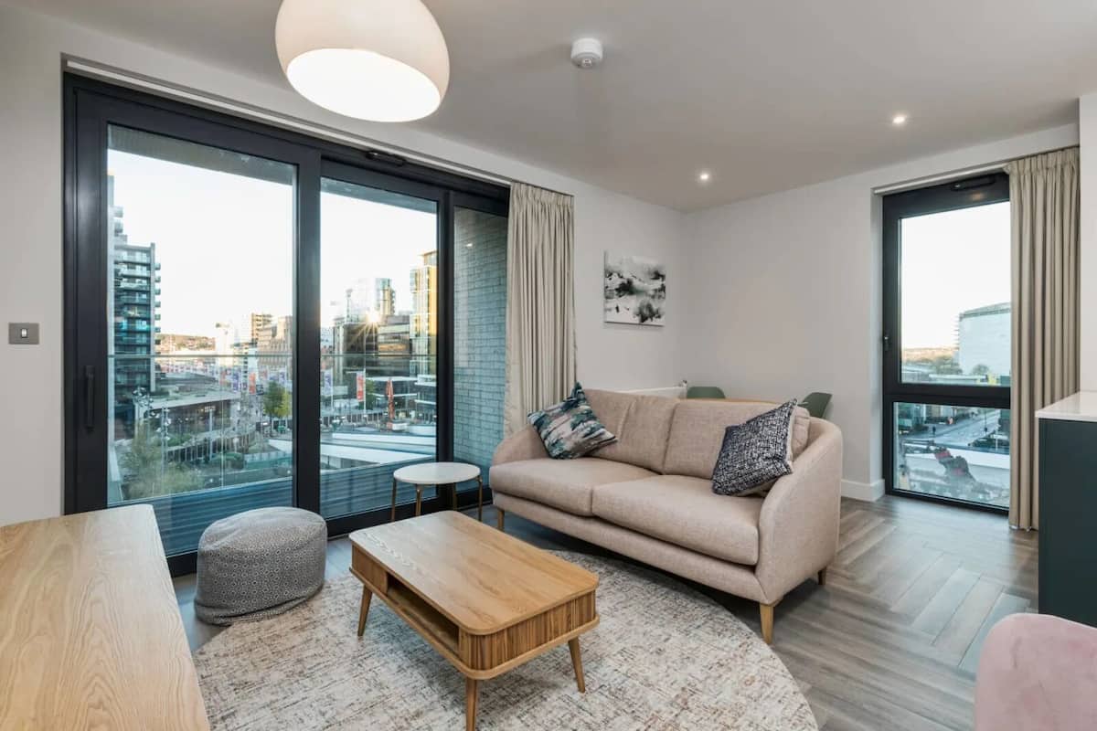 A modern living room with a sofa, coffee table, and a view of the city through large windows.