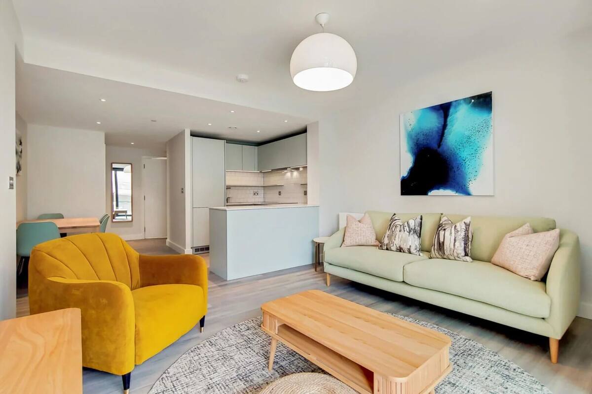 A modern living room with a sofa, a yellow armchair, and a coffee table. There is a kitchen area in the background.