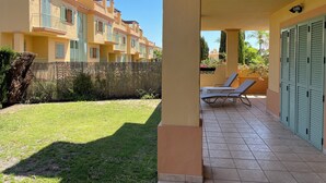 A covered outdoor area with a tiled floor, a grassy lawn, and a row of blue lounge chairs. - Paradise in Marbella, Sea Sun Golf & more Groudfloor apartment with pool access (Marbella benahavis)
