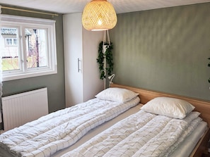 Een slaapkamer met twee enkele bedden, een hanglamp, een radiator en een raam met gordijnen.