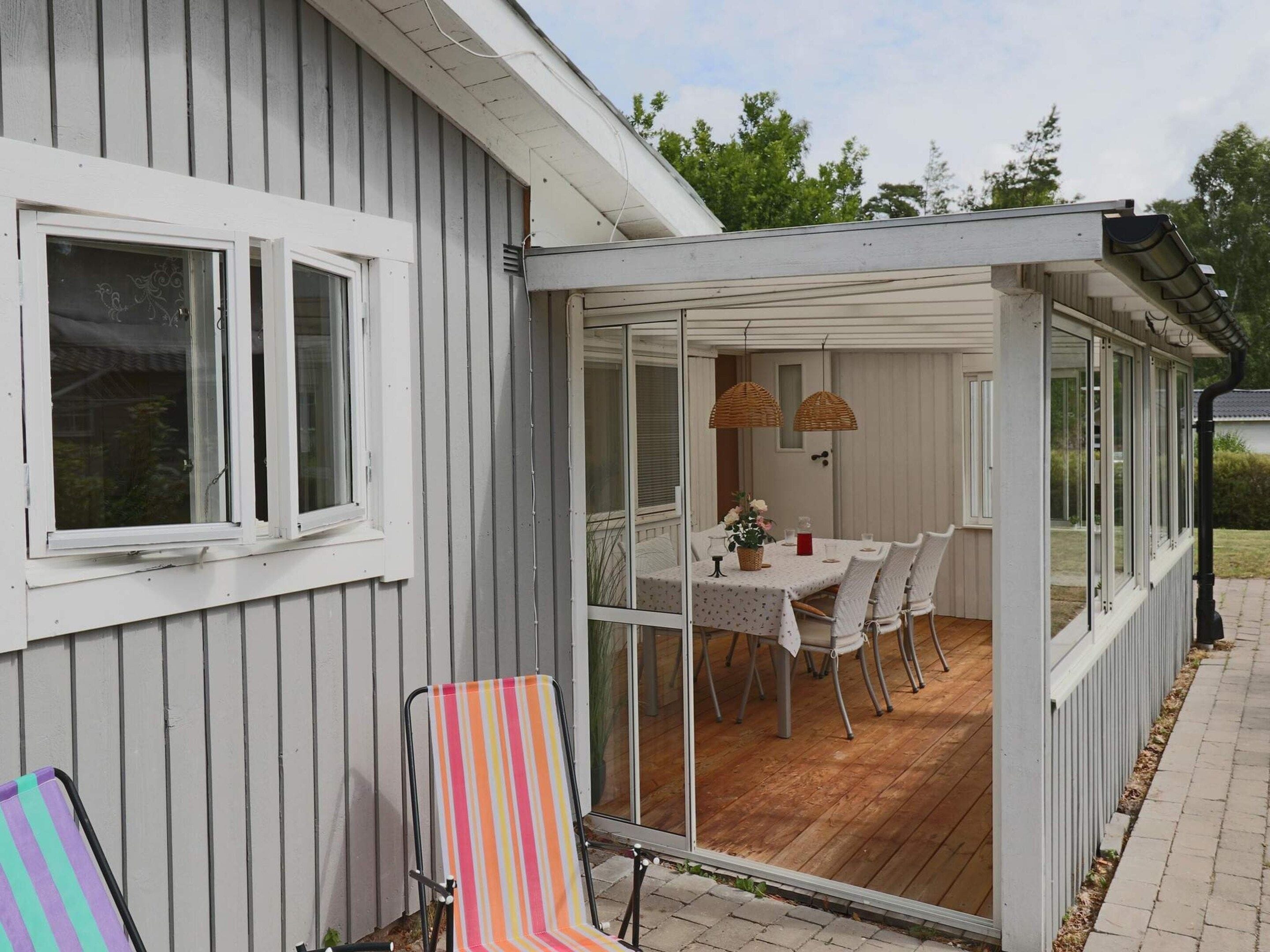 A covered patio with a dining table and chairs, a striped chair, and a window overlooking a garden.