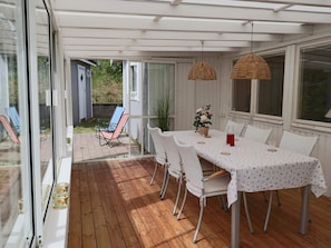 Een terras buiten met een tafel, stoelen en hangende rieten lampen.