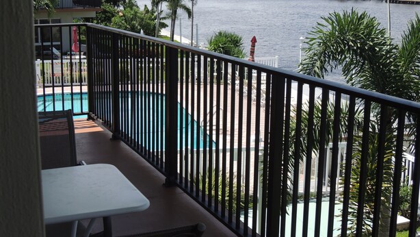 A balcony with a pool, palm trees, and a view of a body of water.