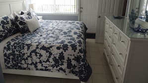 A bedroom with a bed, a dresser, a mirror, and a window with blinds.