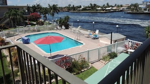 A swimming pool with a red umbrella, surrounded by lounge chairs and a white fence.