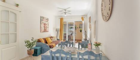 A dining area with a table set for four, chairs with red cushions, and a ceiling fan above.