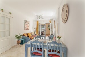 Un comedor con una mesa dispuesta para cuatro personas, sillas con cojines rojos y un ventilador de techo.