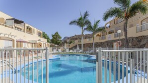 En swimmingpool omgivet af et hvidt hegn, med palmer og et bjerg i baggrunden.