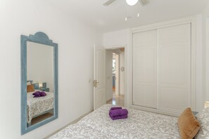 Un dormitorio con cama, un espejo grande, un armario y una puerta que da a otra habitación.