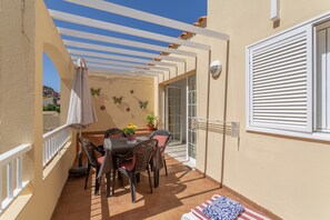 Une terrasse avec une table et des chaises, une plante en pot et un parasol blanc.