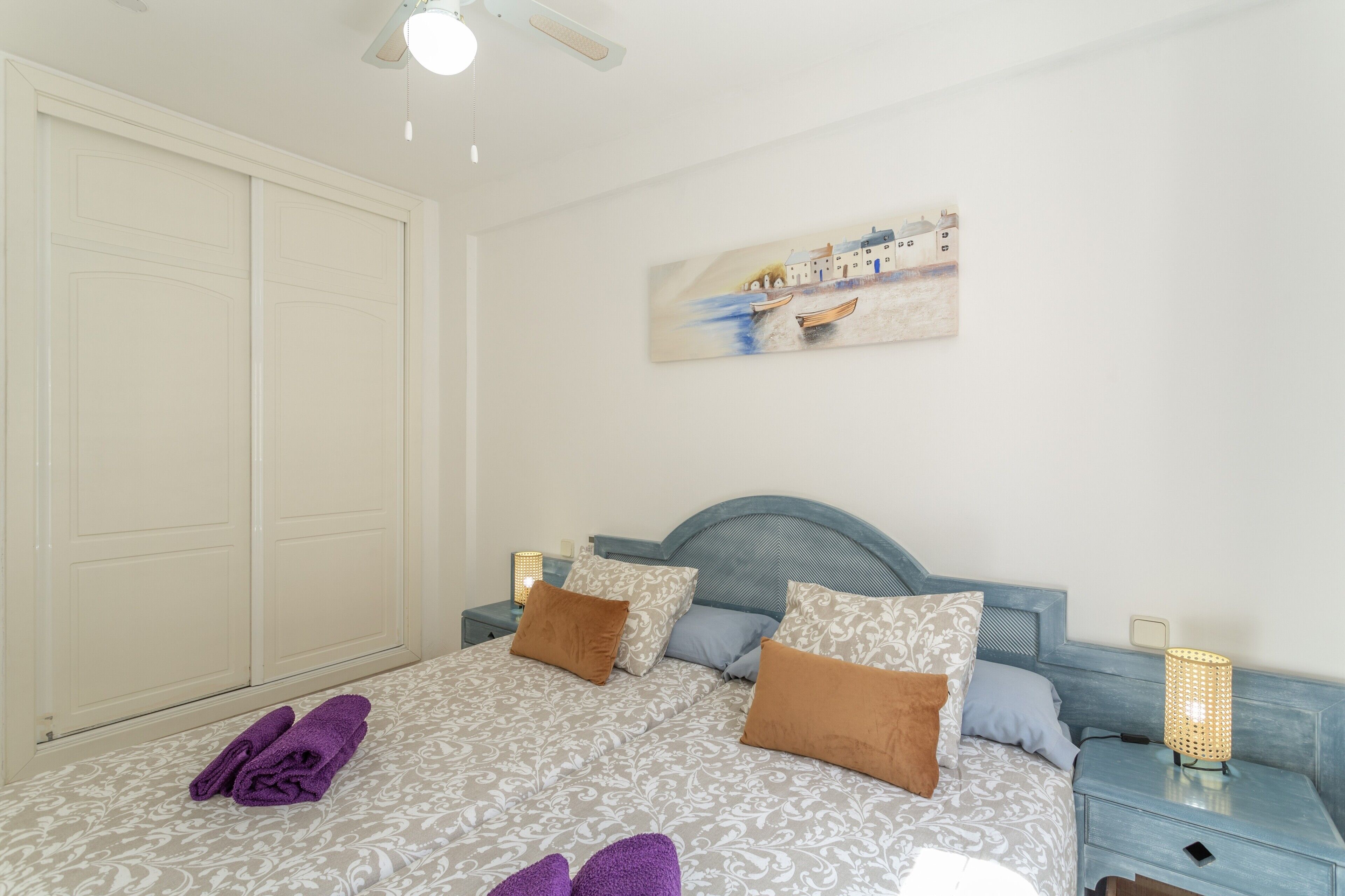 A bedroom with a bed, pillows, a nightstand, a lamp, and a painting on the wall.
