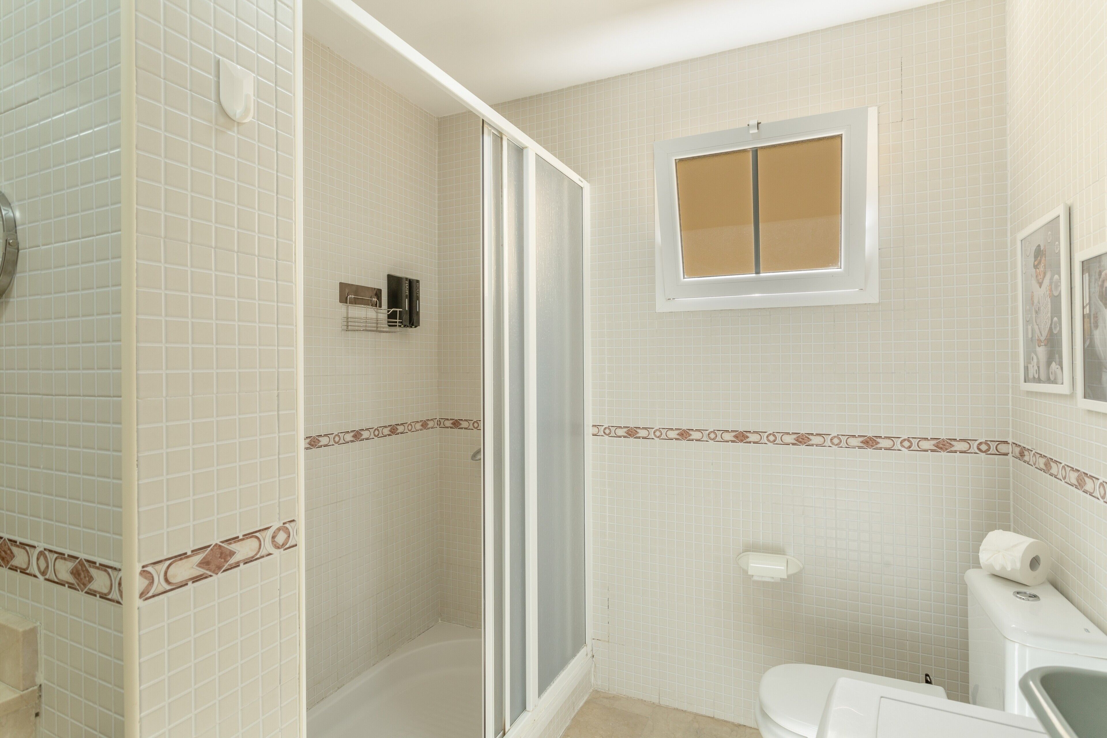 A bathroom with a shower, toilet, and a window.