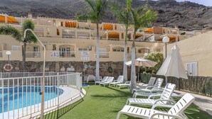 A pool area with artificial grass, lounge chairs, and a view of a mountainous landscape.