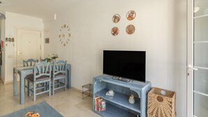 A living room with a dining area, a flat-screen TV, and decorative wall art.