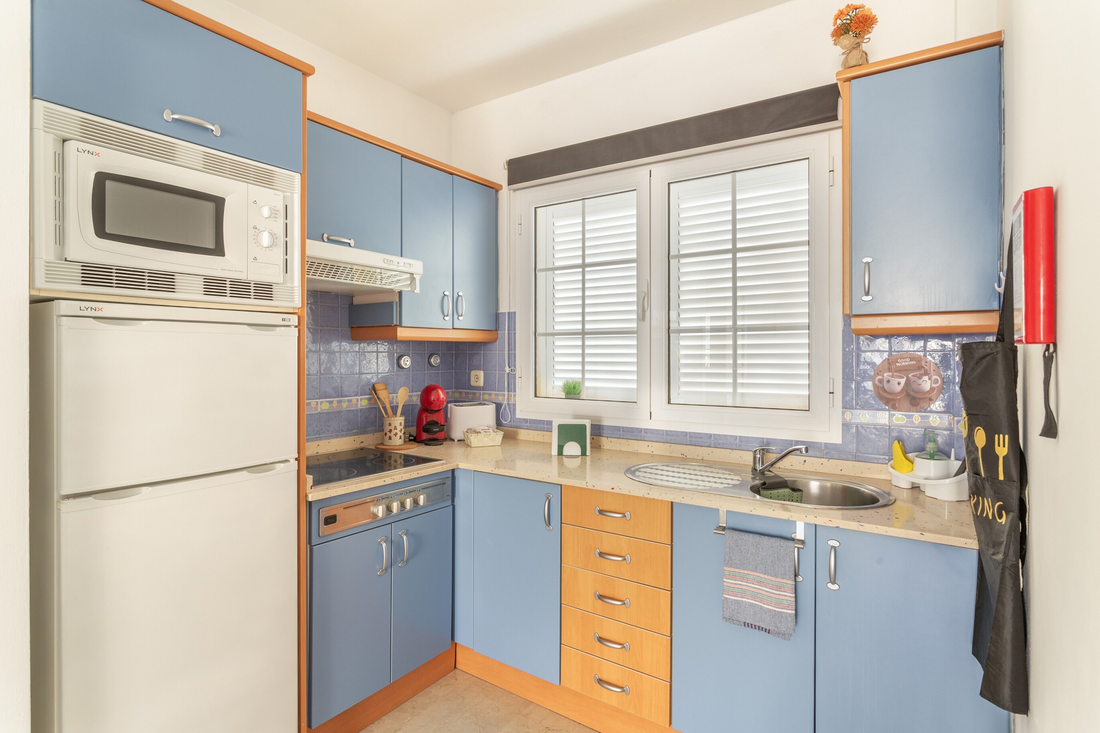 Een keuken met blauwe kastjes, een magnetron, een broodrooster en een spoelbak.