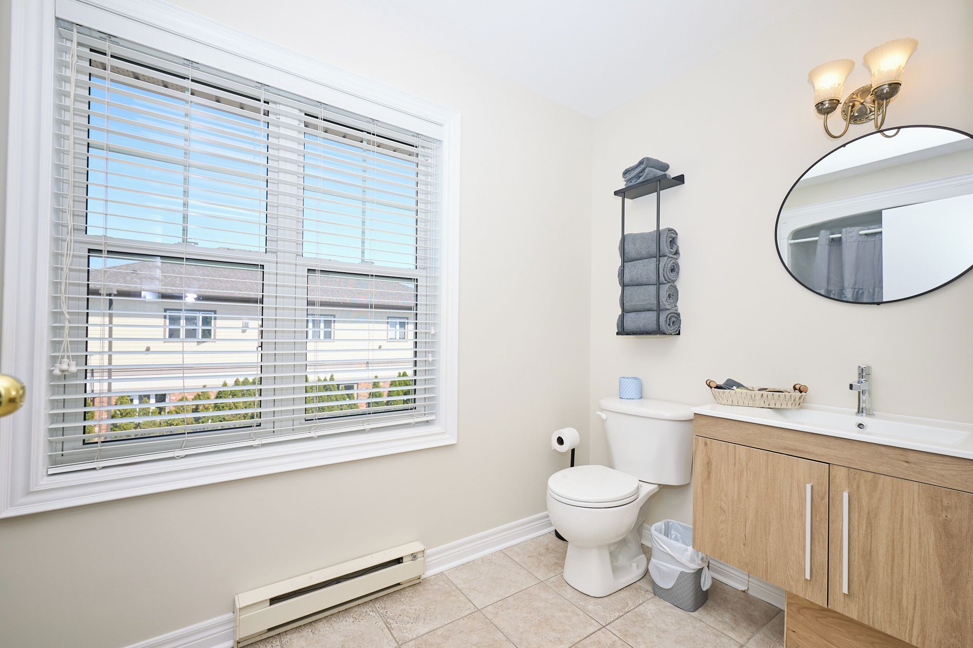 Une salle de bain comprenant des toilettes, un lavabo, un meuble-lavabo et une fenêtre avec des stores.