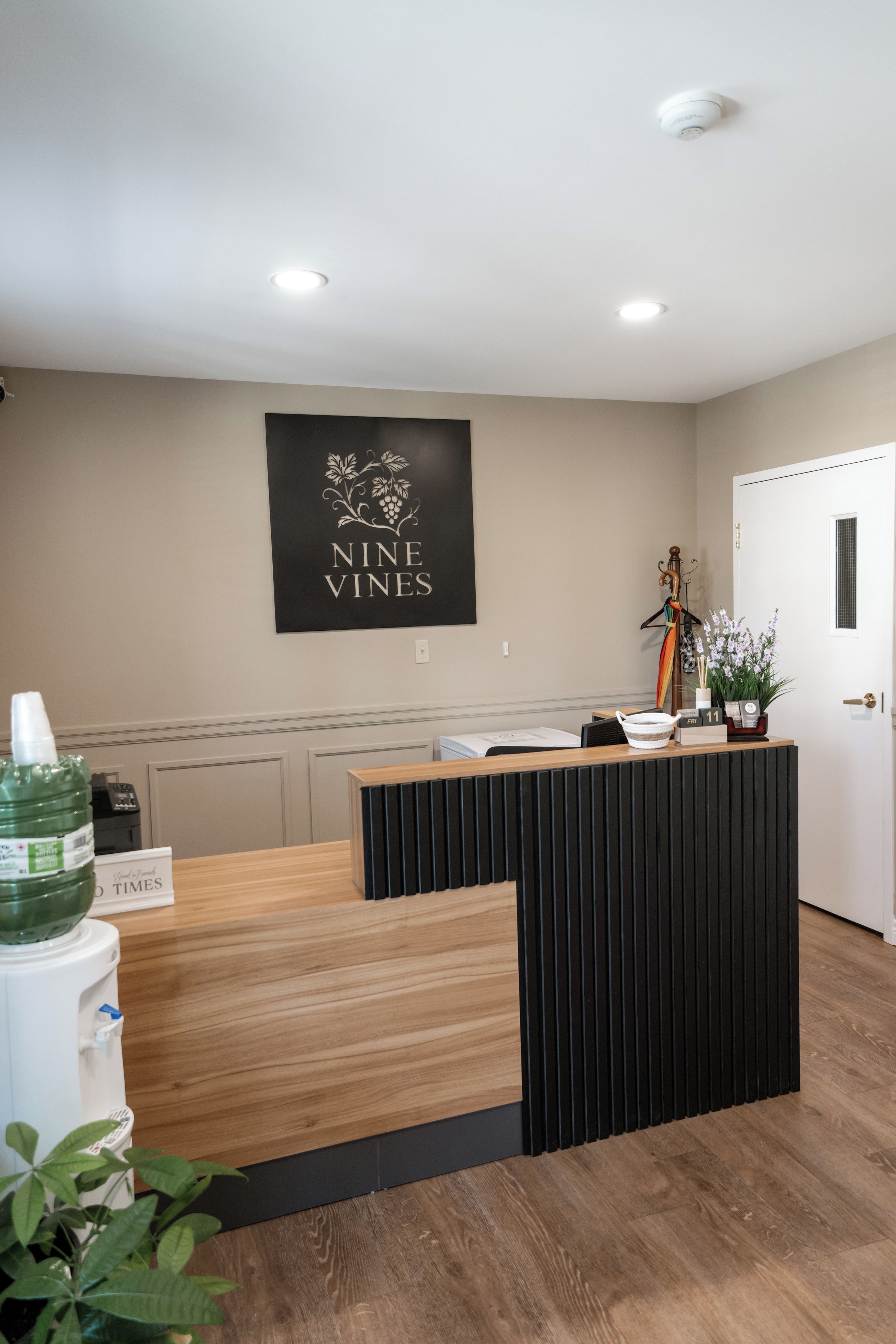 A reception desk with a black and white sign above it, a wooden counter, and a potted plant on the right.