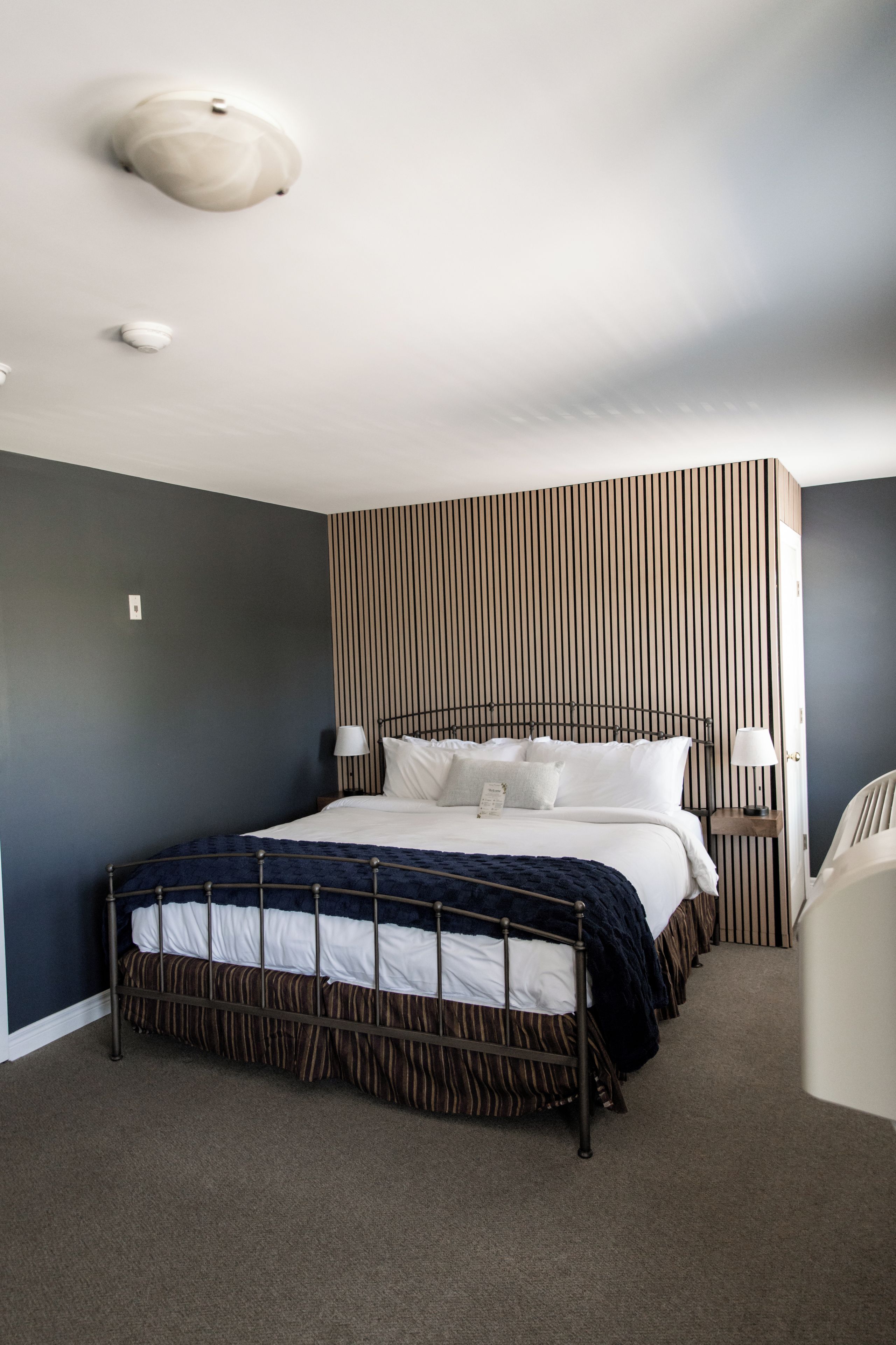 A bedroom with a bed, bedside tables, a wall-mounted light fixture, and a striped wall panel.
