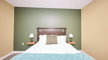Una cama bien hecha con una manta azul, dos lámparas de noche y un cabecero de madera.