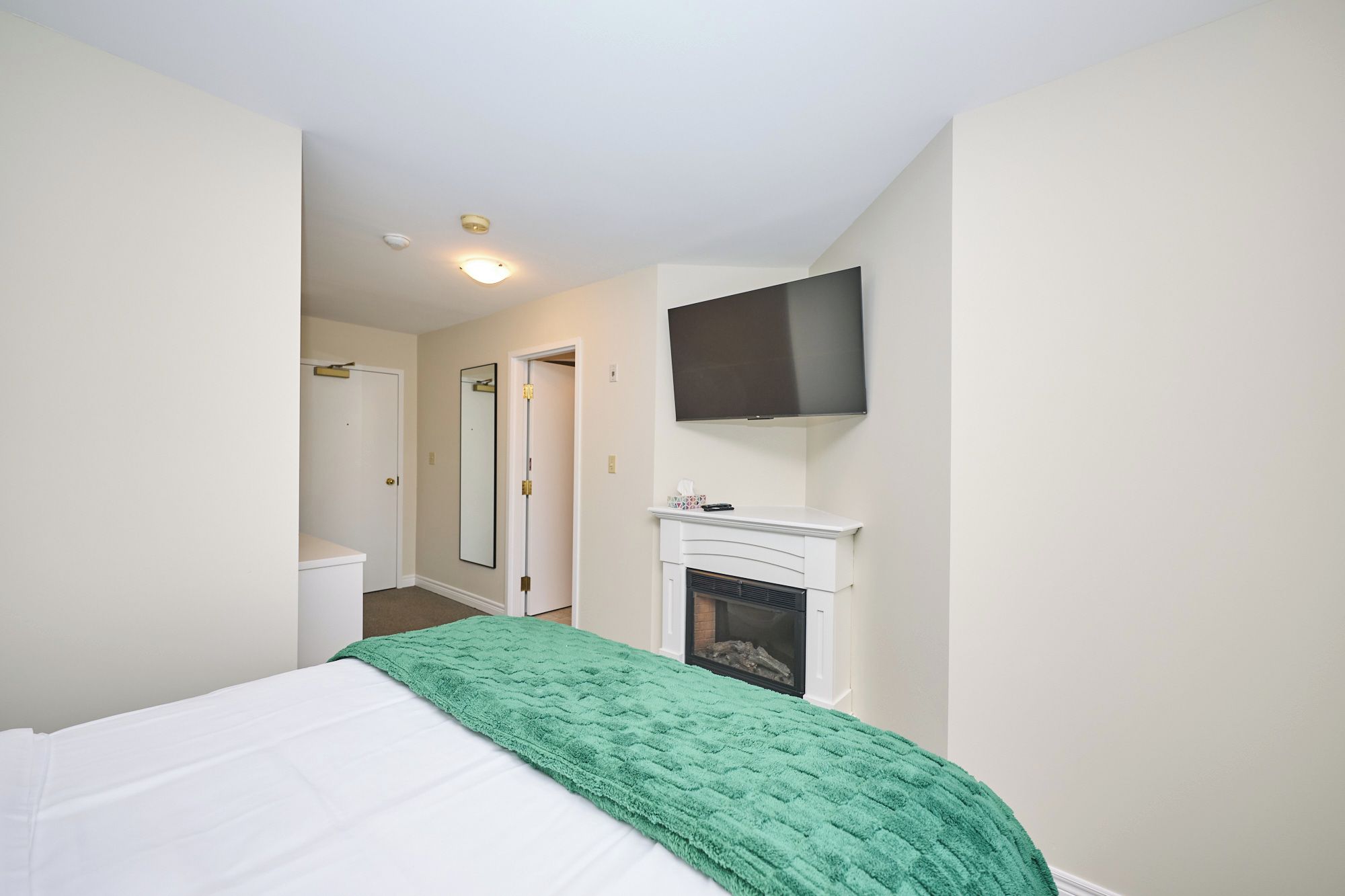 A bedroom with a bed, a green blanket, a fireplace, and a mounted TV.