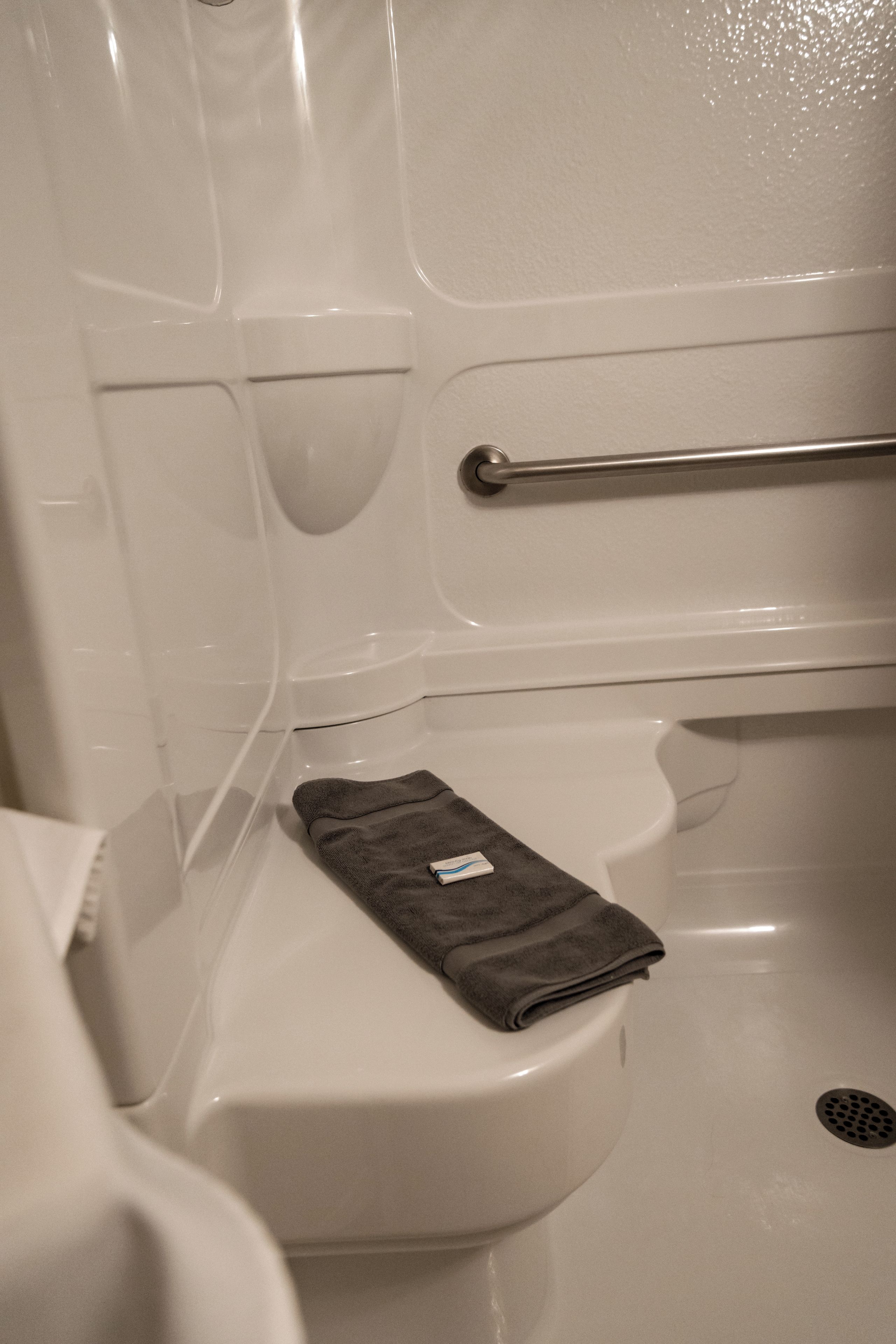 Un baño con inodoro blanco, barra de apoyo metálica y toalla oscura sobre el asiento.