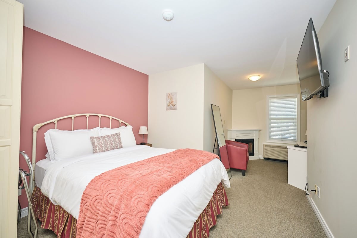Een slaapkamer met een bed, een spiegel, een televisie en een open haard.