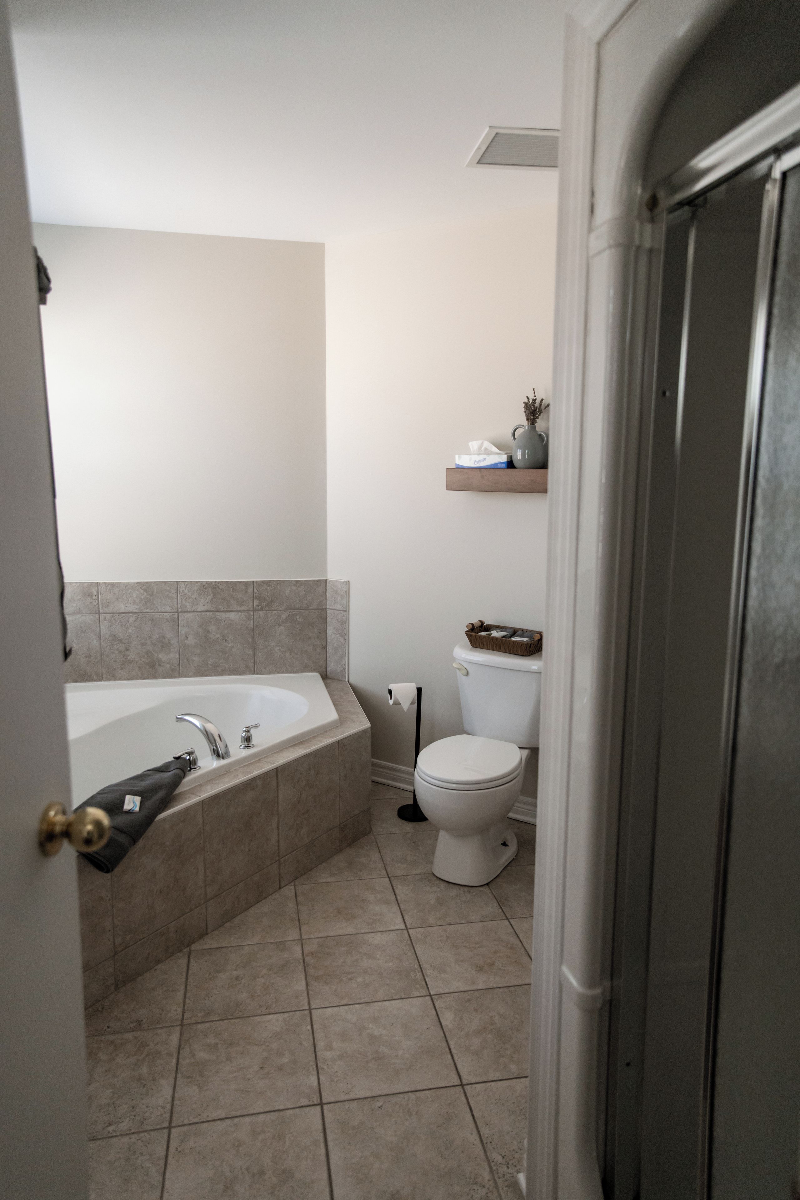 Un baño con bañera, inodoro y un estante con artículos de aseo.