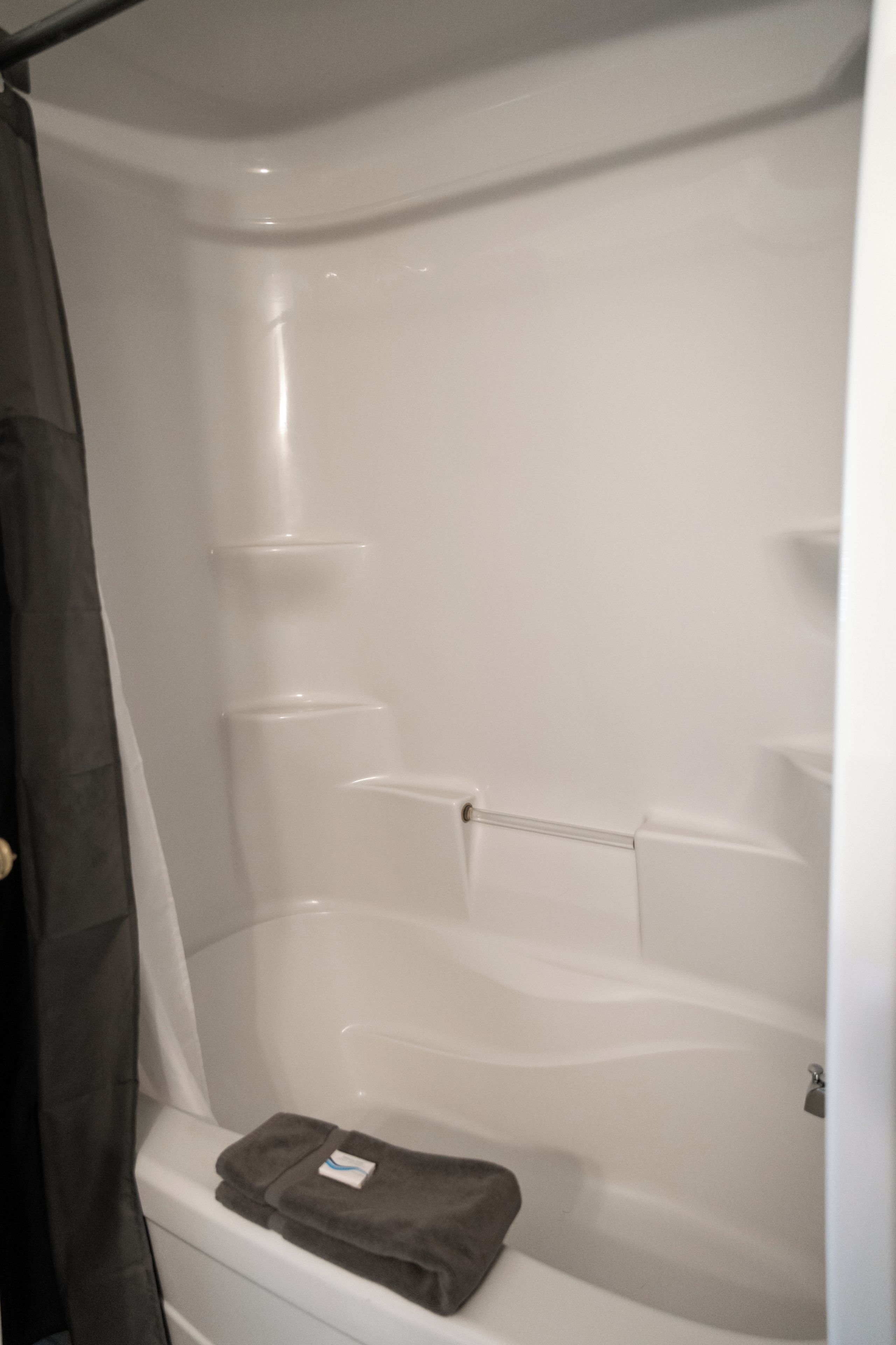Una bañera con cortina de ducha, una toalla y un estante.