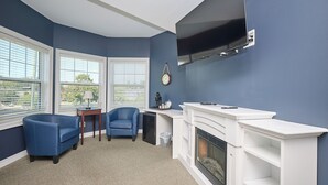 A living room with a fireplace, two blue chairs, a coffee table, and a TV mounted on the wall.