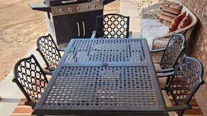Eine Terrasse mit einem Metalltisch und -stühlen, einem Grill und einer gepolsterten Sitzgruppe.