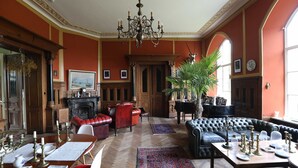 Una habitación amplia con chimenea, un piano, un sofá y una mesa de comedor dispuesta con velas y platos.