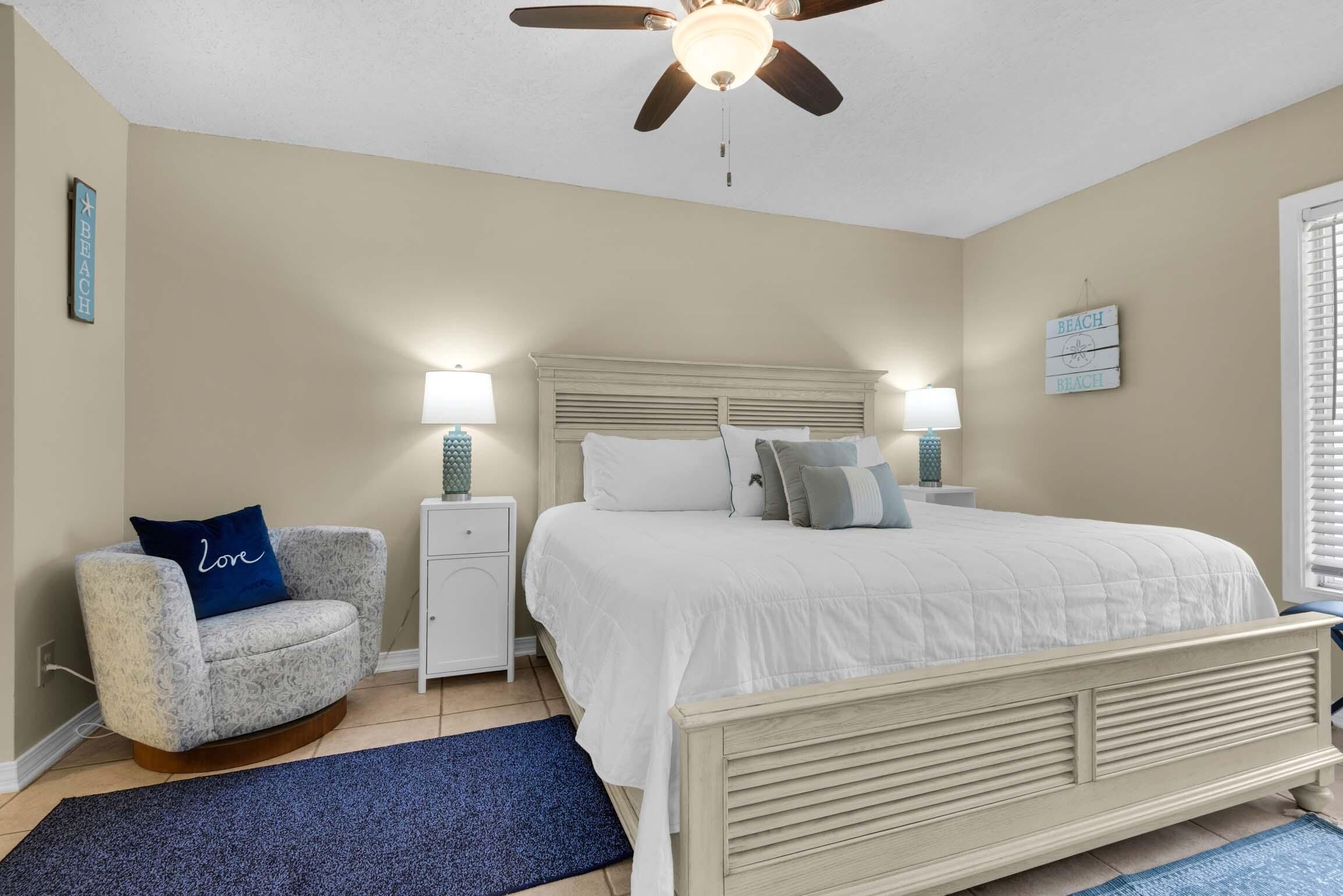 A bedroom with a bed, a chair, a nightstand, a ceiling fan, and wall decorations.