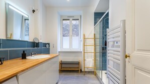 A modern bathroom with a wooden vanity, a large mirror, a window, a glass shower enclosure, and a white door.