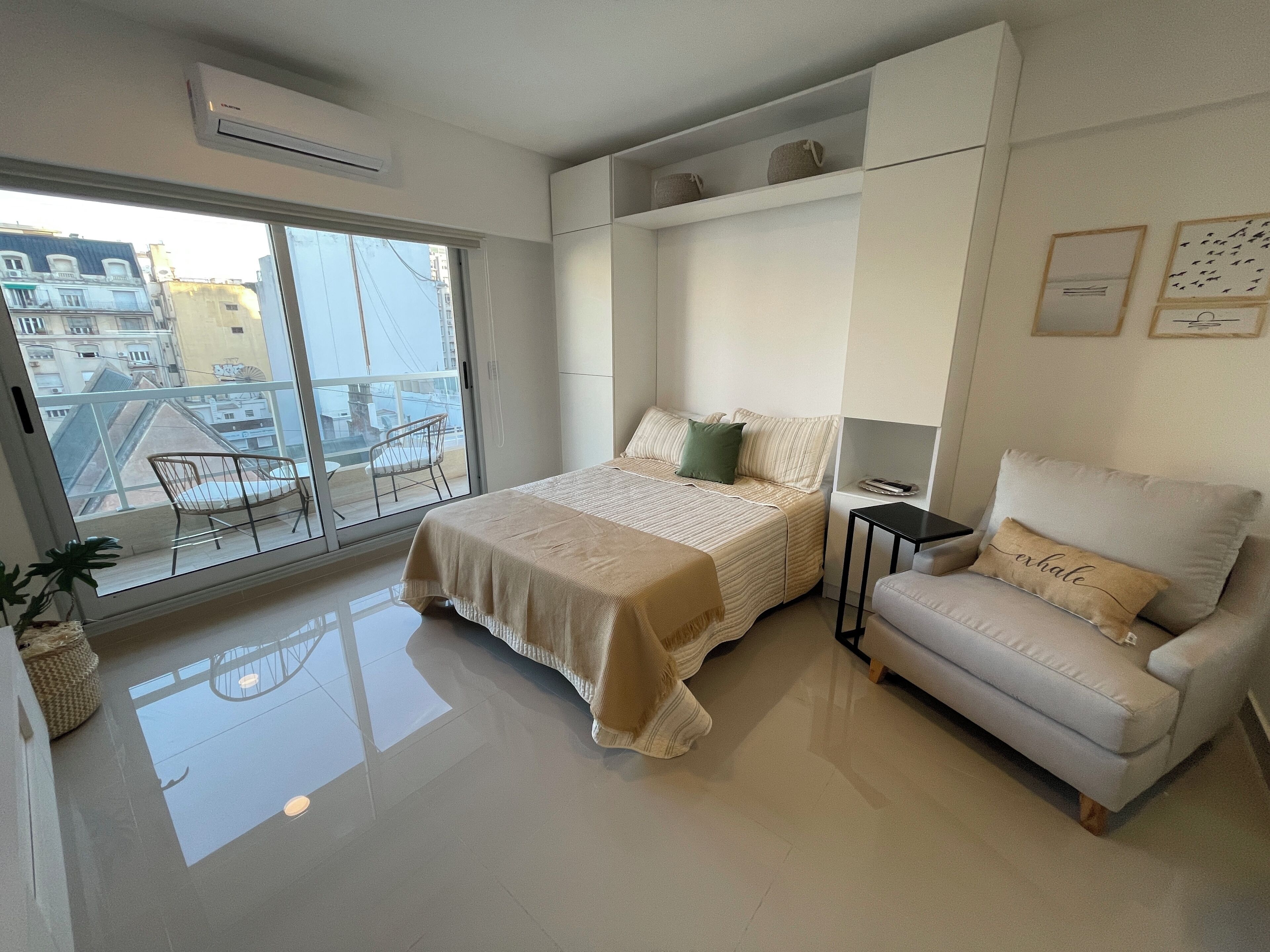 Ein modernes Schlafzimmer mit Bett, Sofa, einem kleinen Tisch und einem Balkon mit Stuhl.